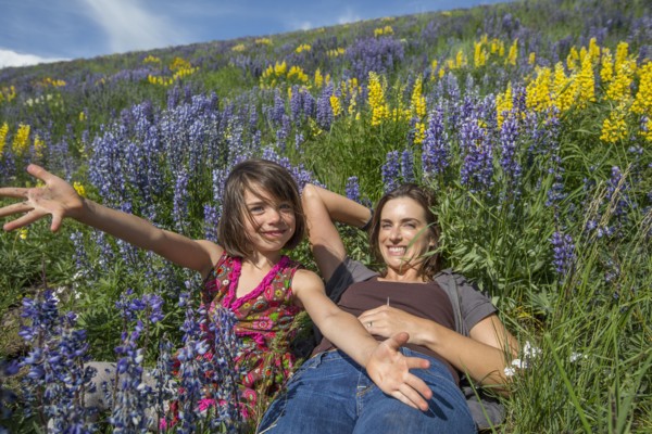 Caucasian mother and daughter on hillside with wildflowers