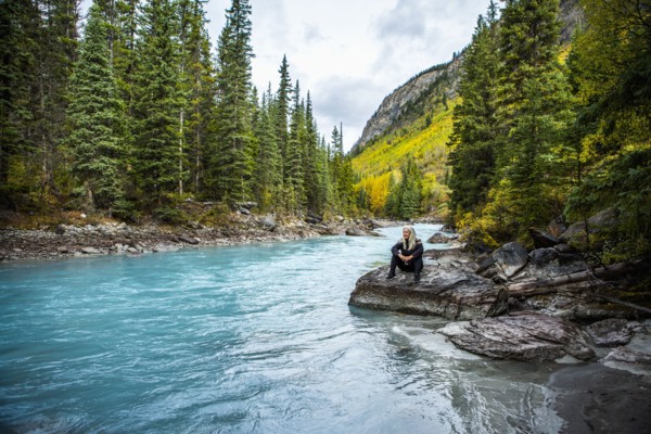 Caucasian woman sitting on rock near mountain river