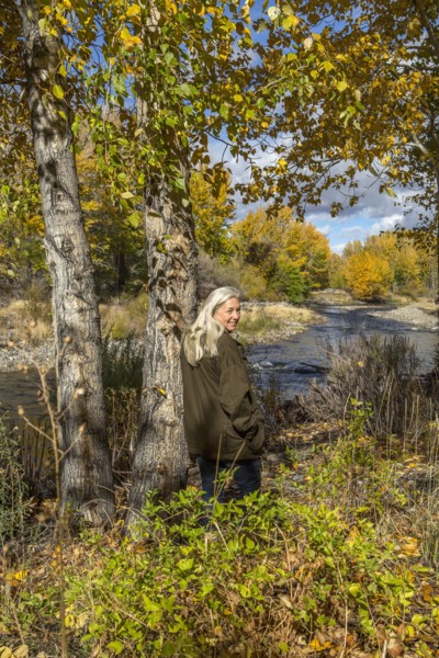 Smiling Caucasian woman leaning on tree near river