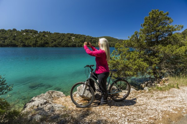Caucasian woman on bicycle photographing lake with cell phone
