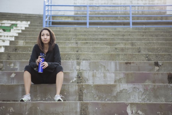 Mixed race woman with water bottle sitting in stadium