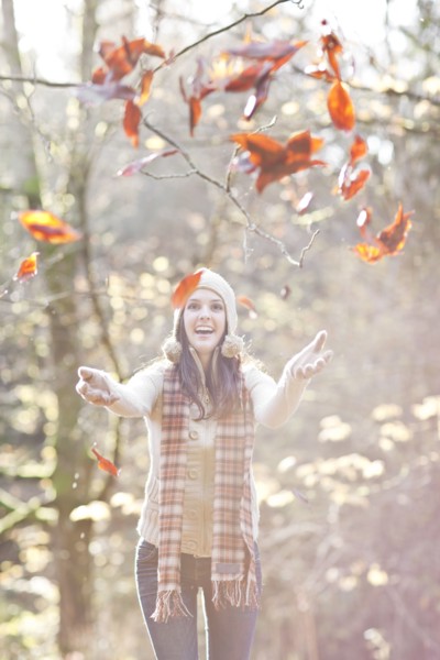 Mixed race woman in cap playing in autumn leaves