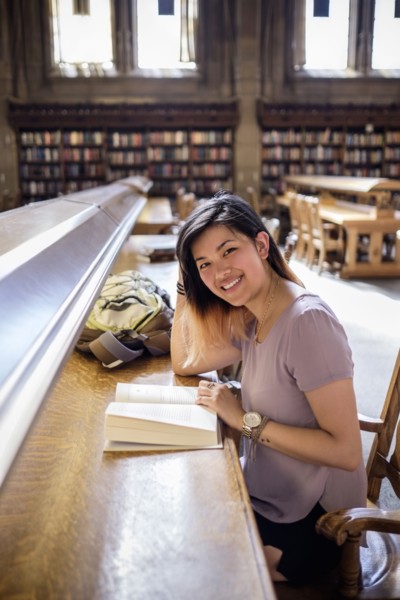 Smiling Chinese woman sitting in library reading book
