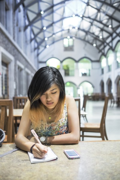 Chinese woman sitting in library writing in notebook