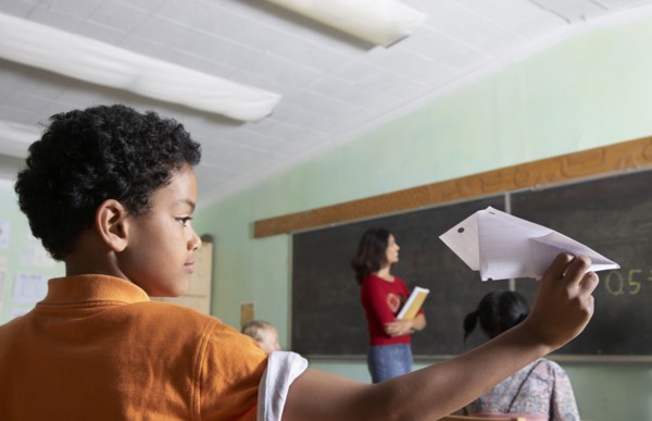 Mixed Race boy throwing paper airplane in class