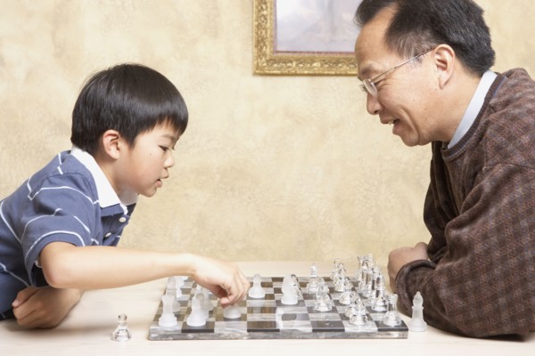 Asian father and young son playing chess
