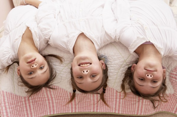 Mixed race girls hanging upside down from bed