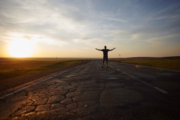 Caucasian man standing in cracked road at sunset with arms outstretched