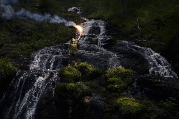 Caucasian girl holding smoke flare near waterfall