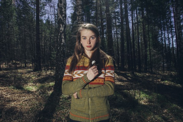 Serious Caucasian woman holding flower in forest