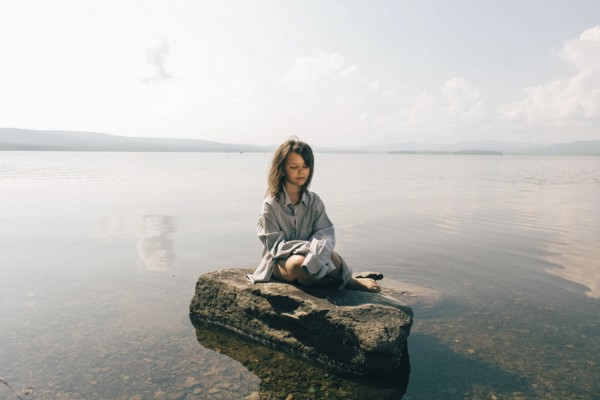 Caucasian girl sitting on rock in lake