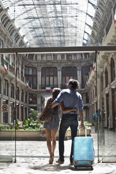 Caucasian couple pulling luggage into ornate building