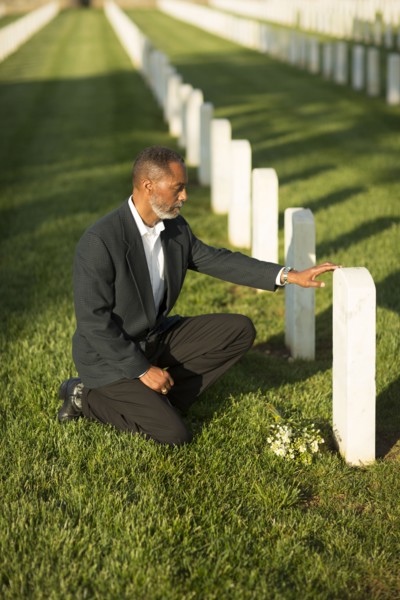 Black man kneeling with bouquet at military cemetery