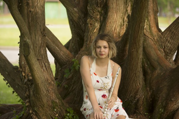 Caucasian teenage girl sitting on tree root holding flute