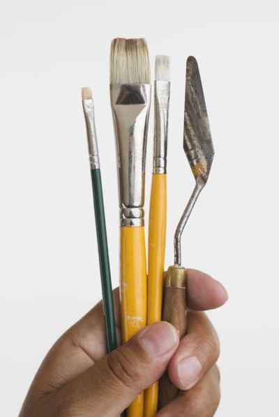 Close up of hands holding paintbrushes and palette knife