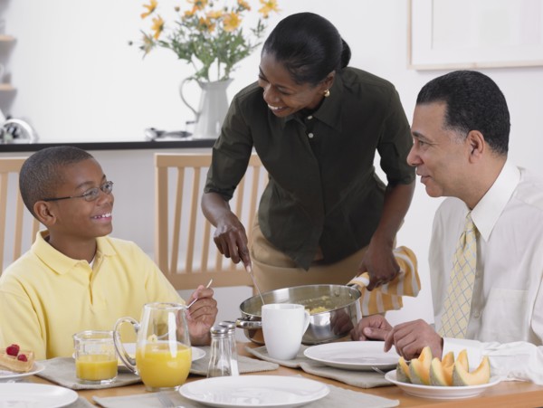 African woman serving breakfast to husband and son