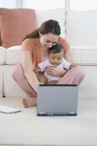 Hispanic mother using laptop with baby in lap