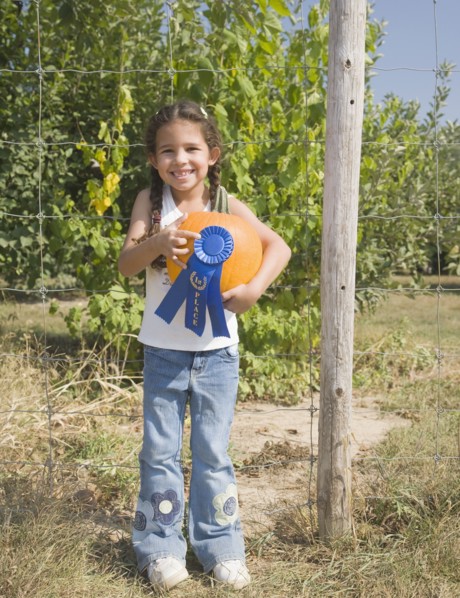 Hispanic girl holding pumpkin with blue ribbon