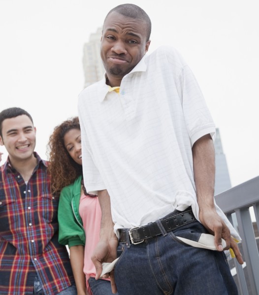 African man showing empty pockets with friends in background