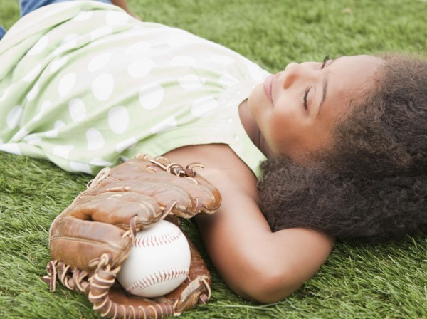 Mixed race girl laying next to baseball glove and ball