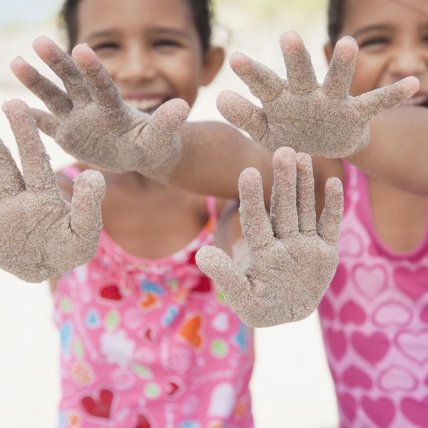Hispanic sisters displaying sand-covered hands