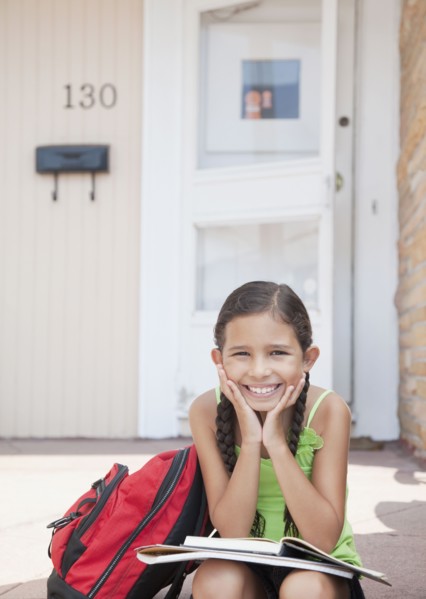 Hispanic girl sitting with school books on front stoop