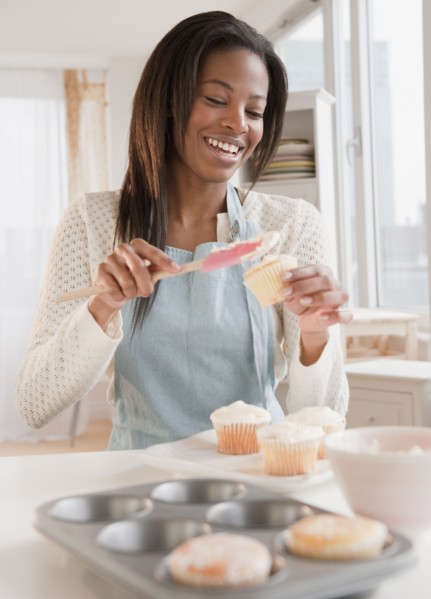 Mixed race woman spreading frosting onto cupcakes
