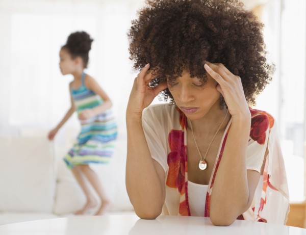 Mother with headache and daughter jumping on sofa