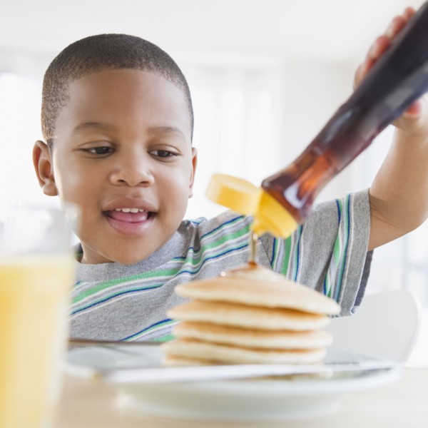 African American boy pouring syrup on pancakes