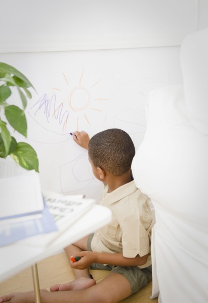 African American boy drawing on wall with crayon