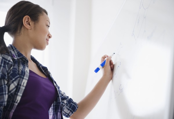 Mixed race teenage girl writing on whiteboard in classroom