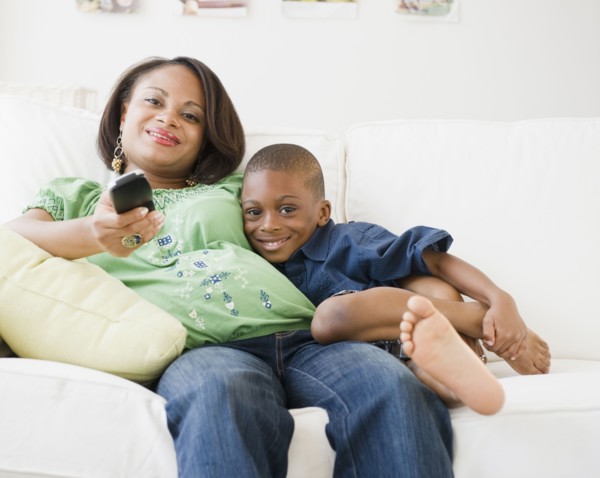 Black mother and son watching TV on living room sofa