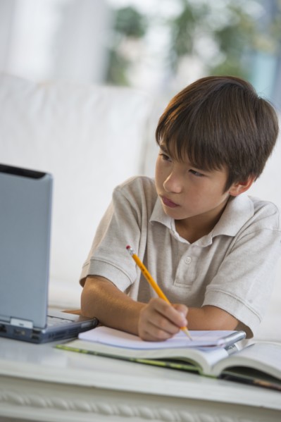 Mixed race boy doing homework and looking at laptop
