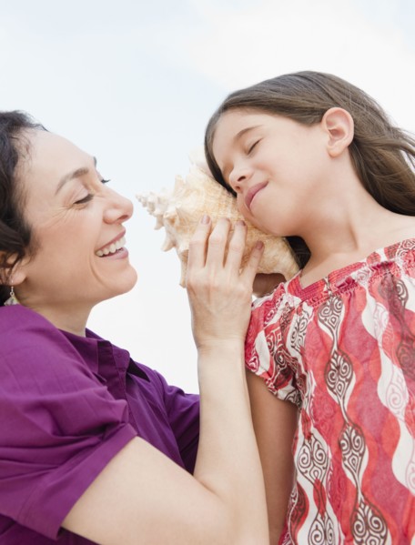 Mother holding seashell to daughter's ear