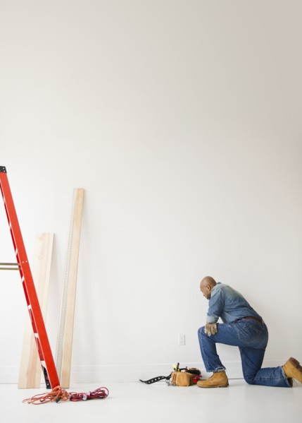 African American construction worker kneeling to look at wall