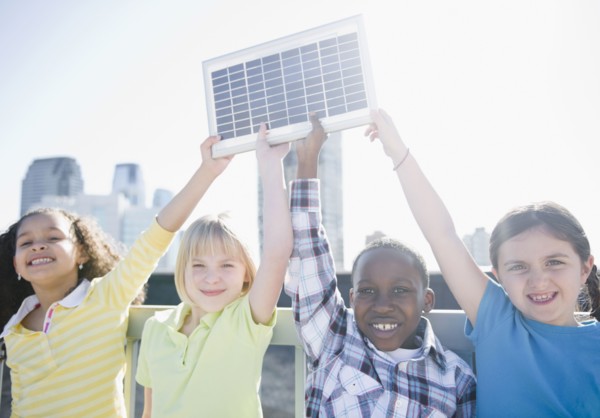 Children on rooftop holding up solar panel