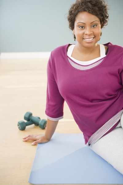 African woman sitting on yoga mat with dumbbells