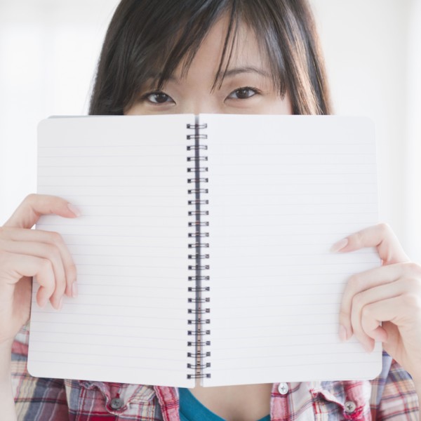 Korean woman holding notebook on front of her face