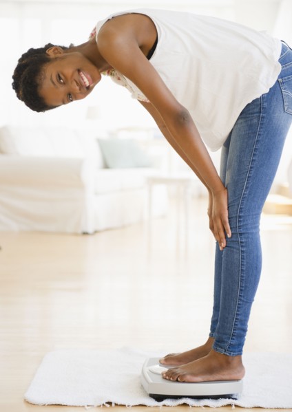 Smiling Black woman weighing herself