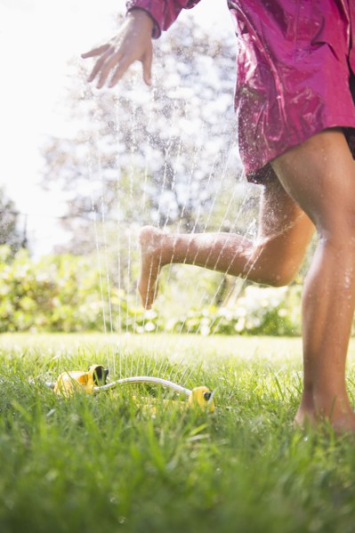 Hispanic girl running through sprinkler