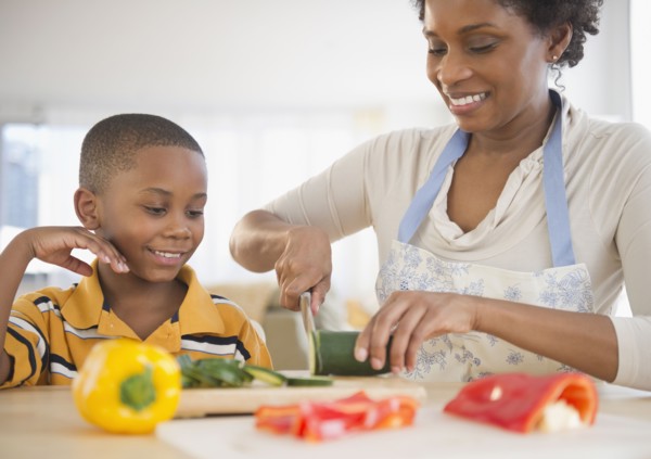 Black son watching mother slicing vegetables
