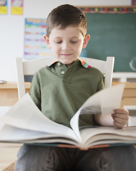 Caucasian boy reading book in classroom