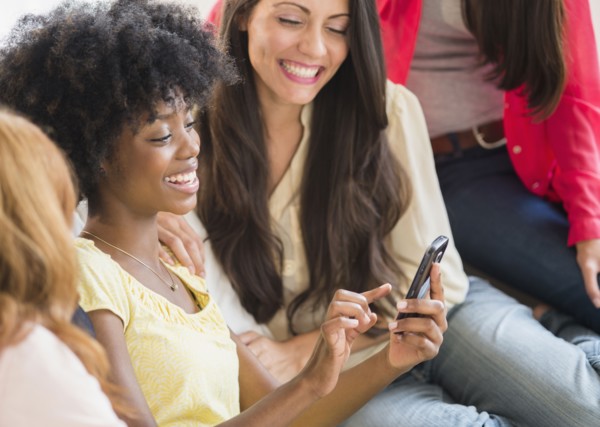 Women using cell phone together on sofa