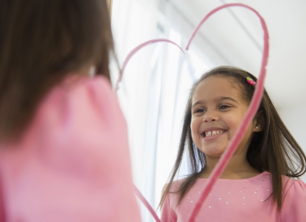 Hispanic girl making lipstick heart in mirror