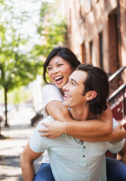 Man carrying girlfriend piggyback on urban sidewalk