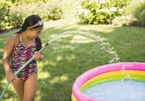 Mixed race girl filling wading pool in backyard