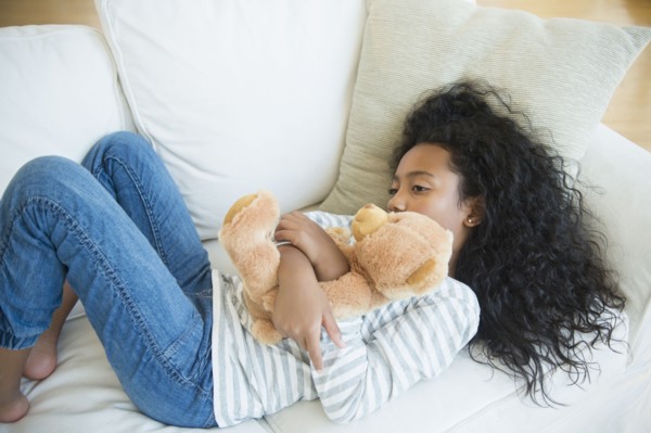 Mixed race girl hugging teddy bear on sofa