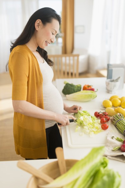 Pregnant Japanese woman slicing vegetables in kitchen
