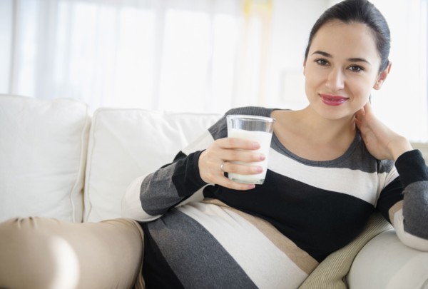 Pregnant Caucasian woman drinking milk on sofa