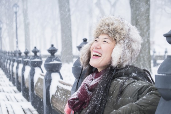 Asian woman sitting on park bench in snow
